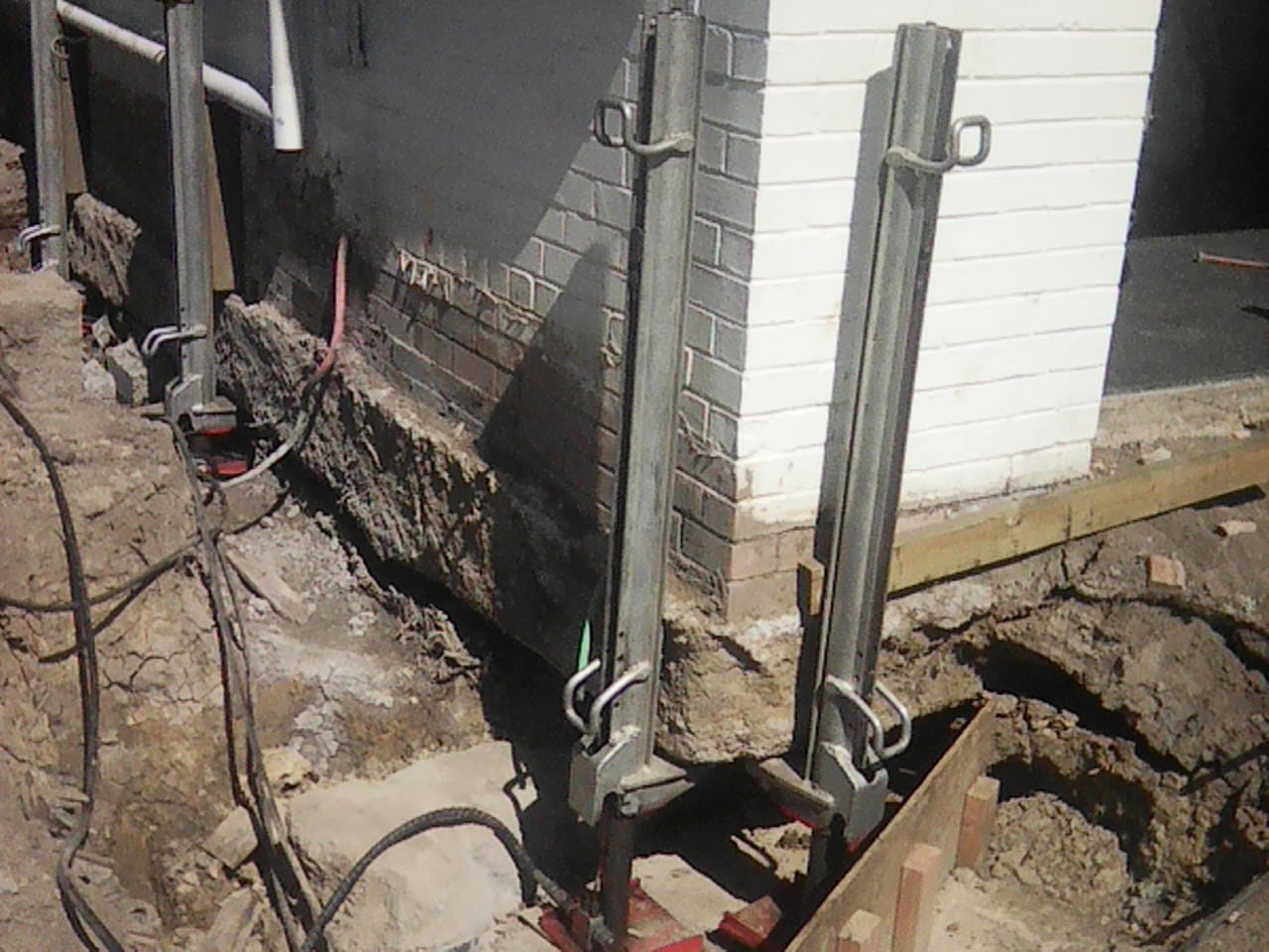 house-lifting-hydraulic-jacks-foundation-repiling Hydraulic jacks installed beneath a house for lifting and foundation re-piling work