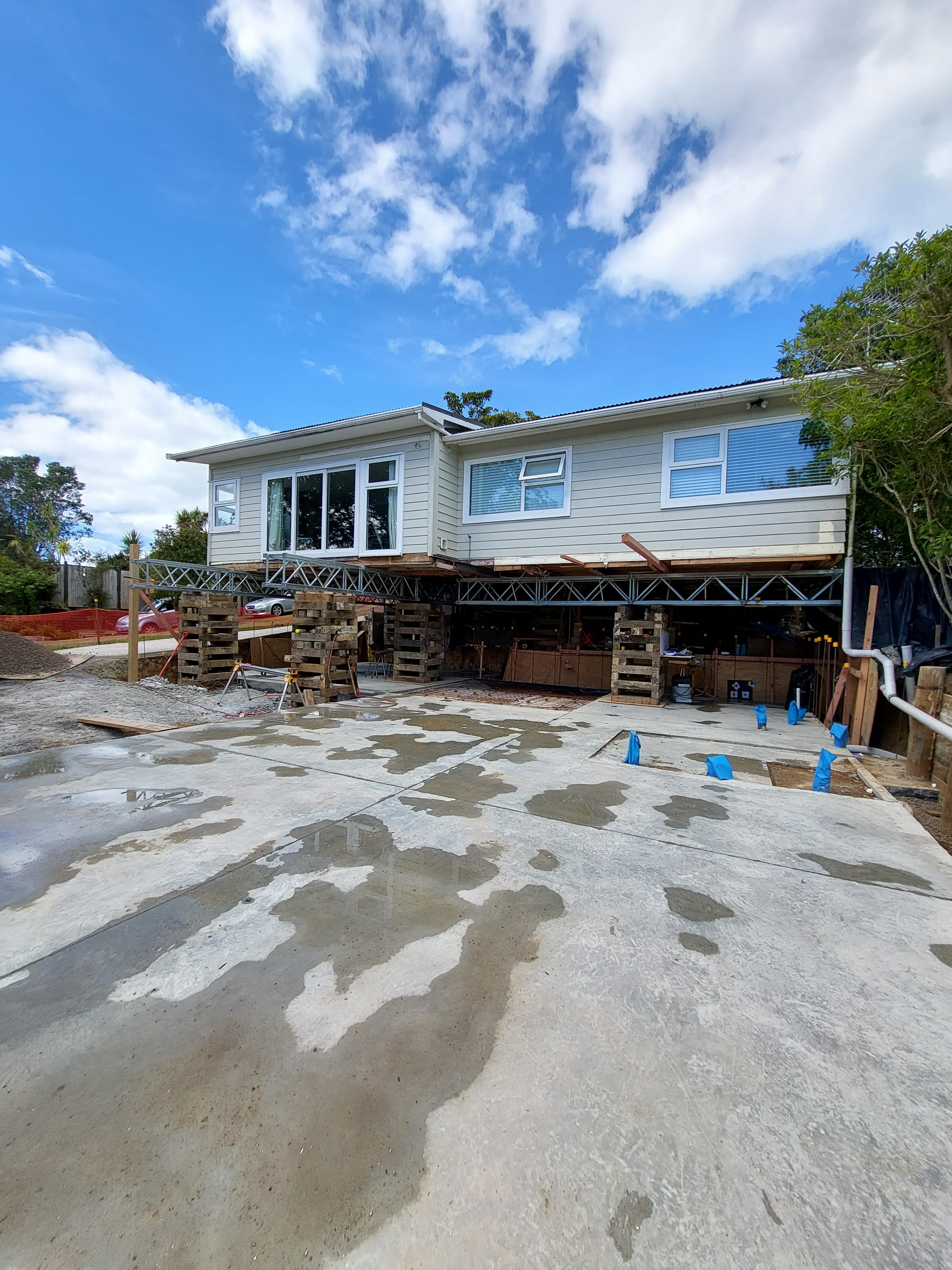 House lifted on steel beams and timber cribbing above a newly poured concrete slab