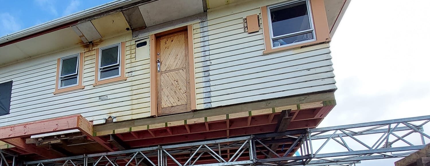 House lifting process with residential building elevated on steel beams and temporary supports during foundation work