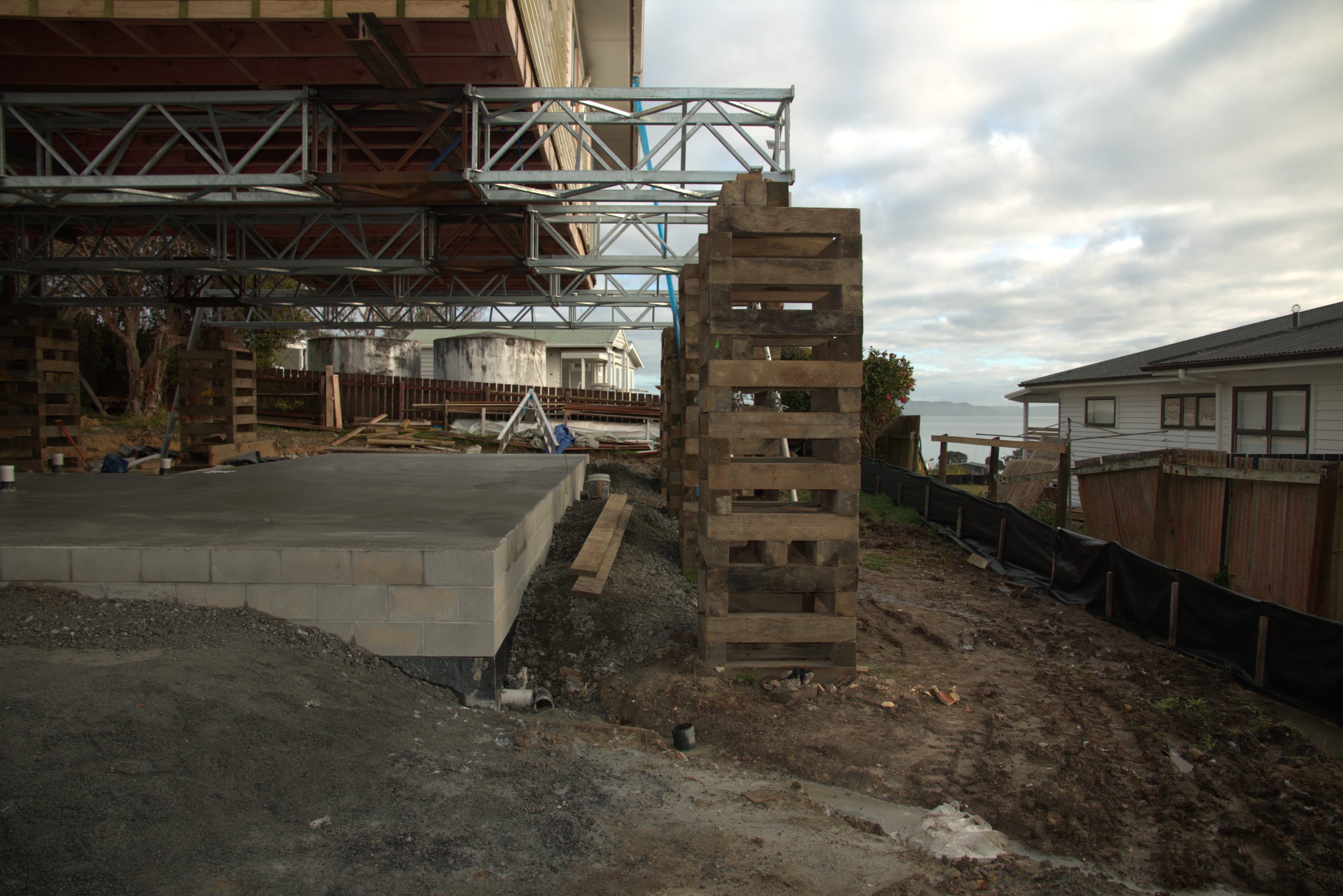 house-lifting-steel-trusses-concrete-slab-support House lifted on steel trusses with timber cribbing beside a newly constructed concrete slab foundation