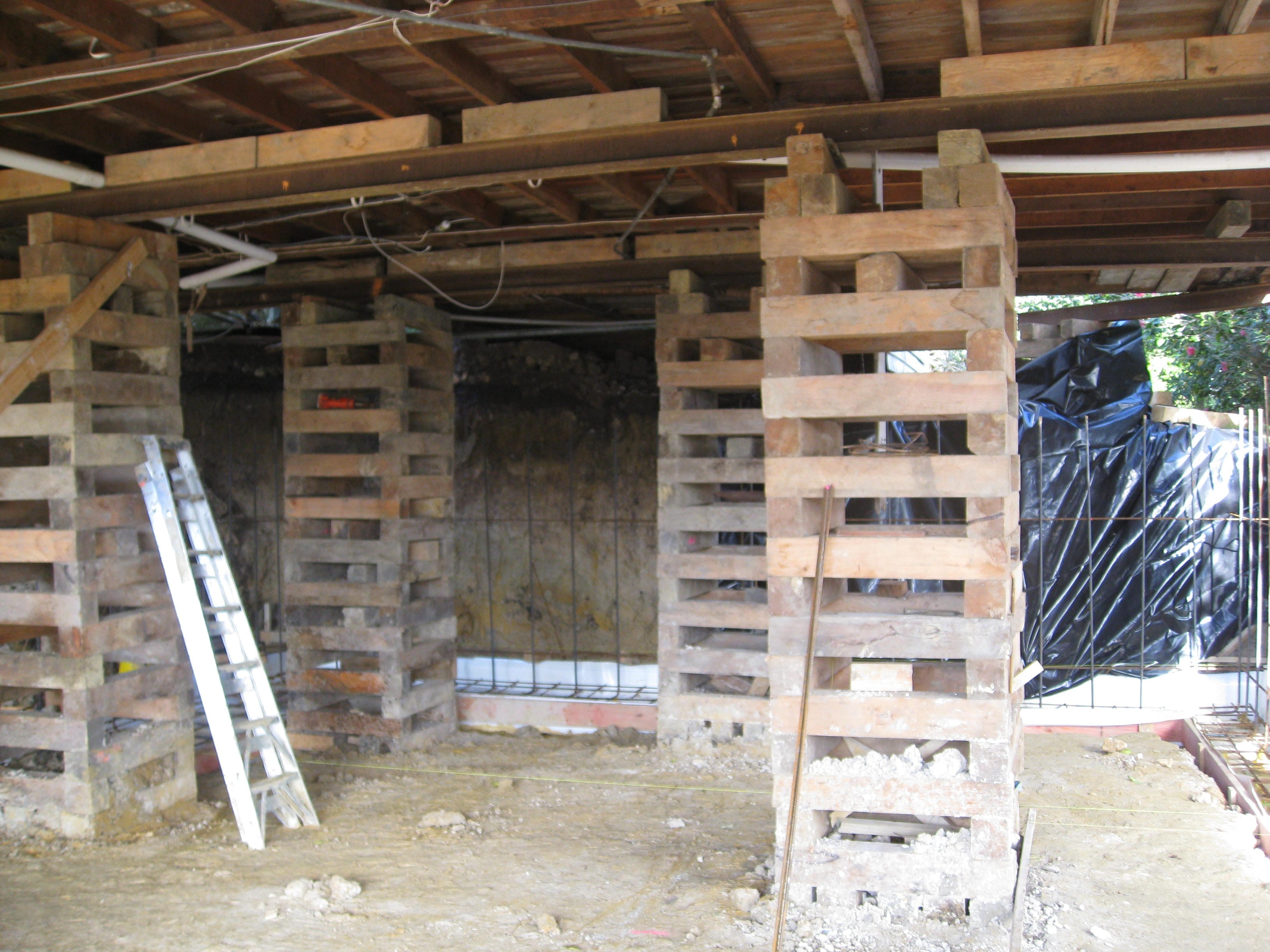 Timber cribbing stacks supporting a house during lifting, with exposed underfloor beams and temporary bracing