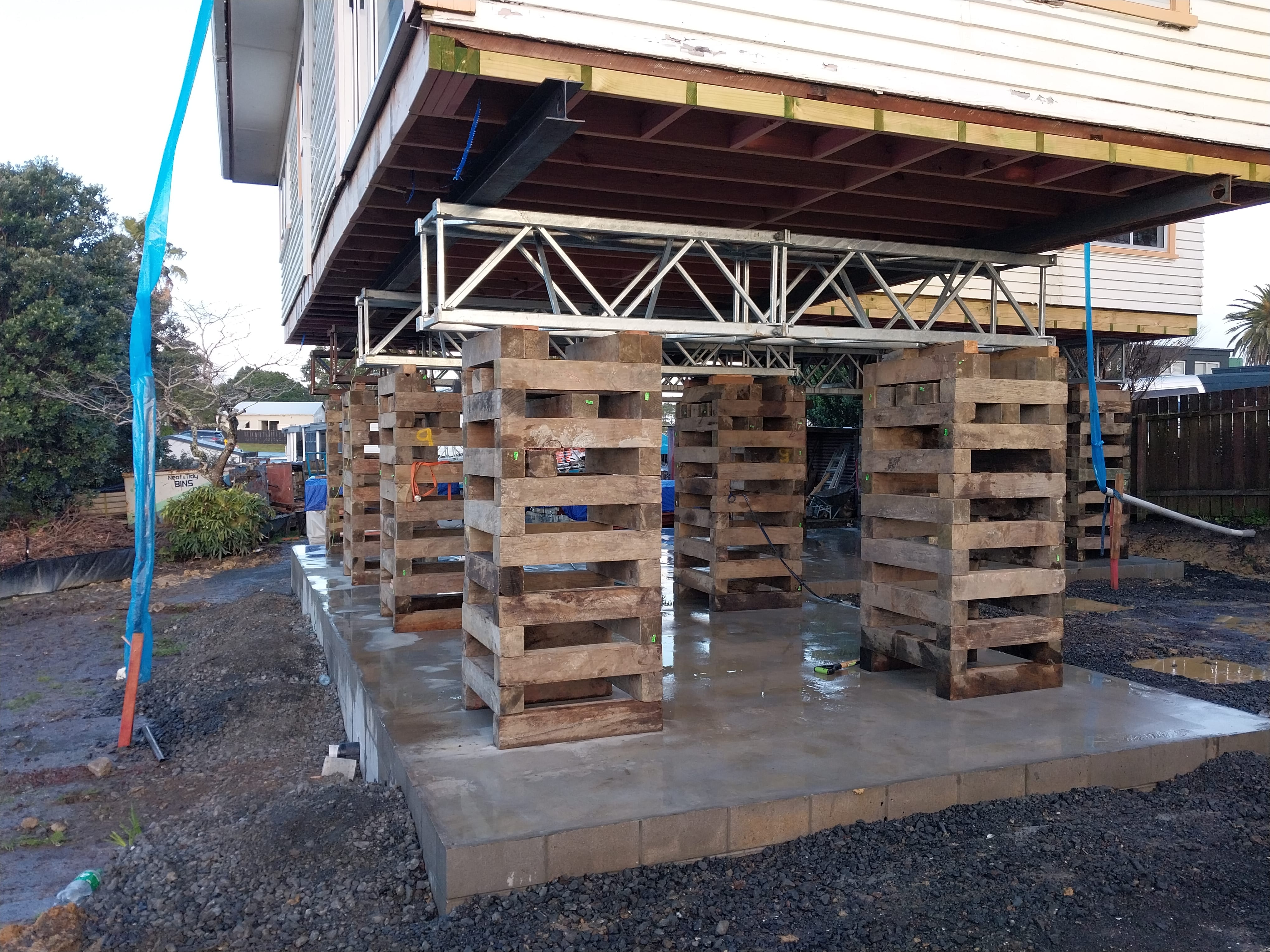 House lifting supported by timber cribs and steel frame above a newly constructed concrete foundation
