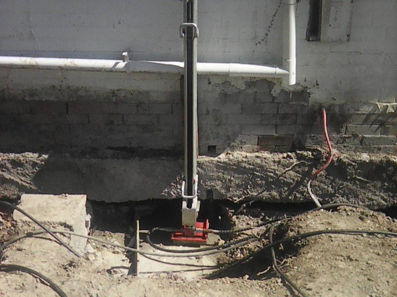 house-repiling-hydraulic-jack-foundation Hydraulic jack installed beneath a house during repiling work, supporting the foundation while ground excavation is underway