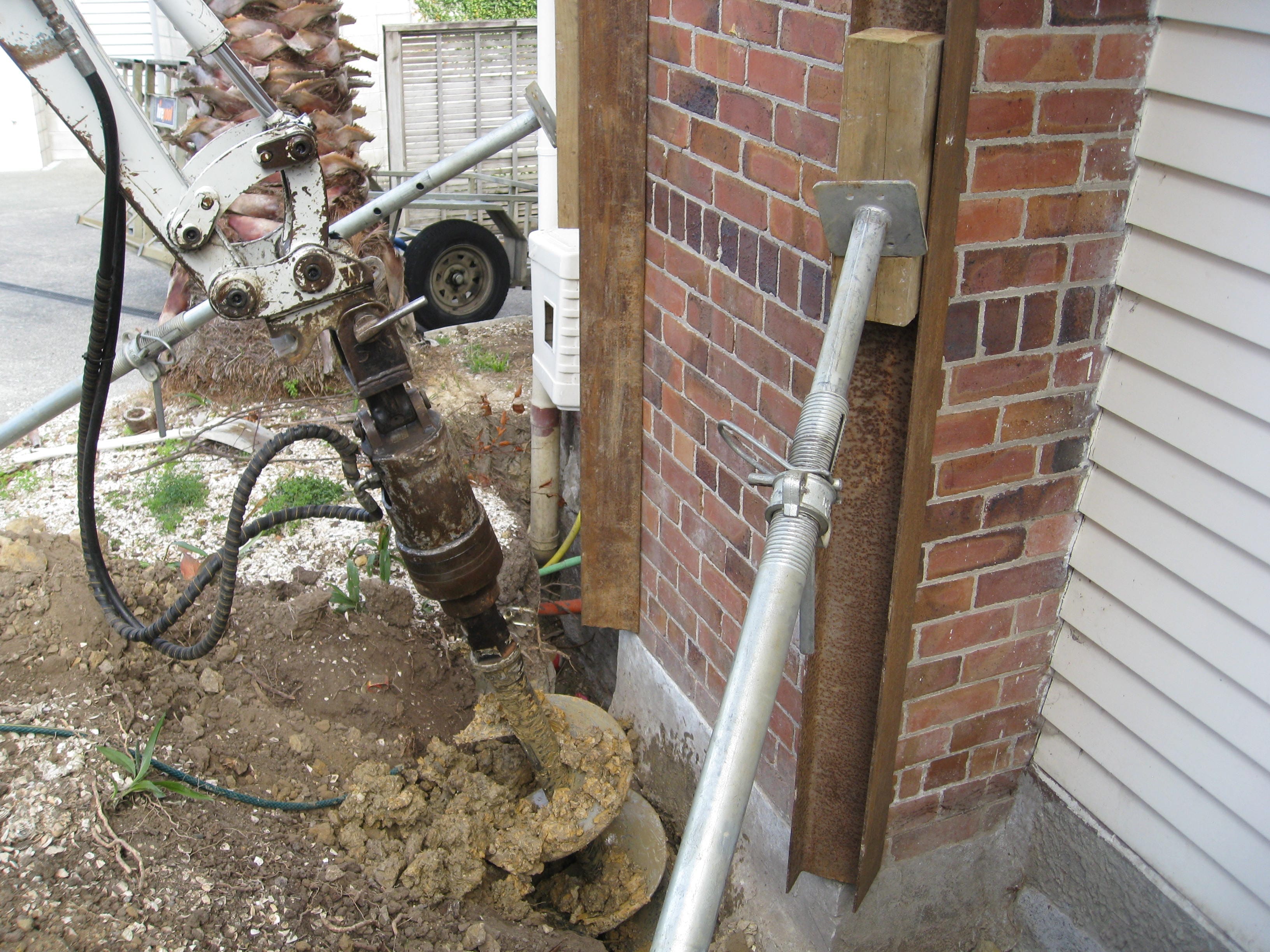 Screw pile installation beside a house for foundation stabilisation and structural support